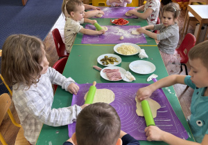 Dzieci siedzą przy stole i formują ciasto na pizzę.