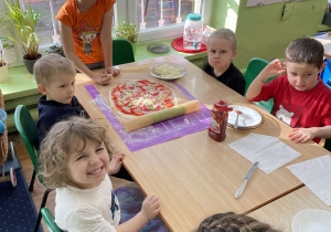 Dzieci siedzą przy stole na którym leży przygotowana pizza.