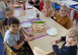 Dzieci siedzą przy stole na którym leży przygotowana pizza.