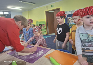 dzieci w kolorowych chustkach na głowie, przy stolikach, samodzielnie przygotowują pizzę.