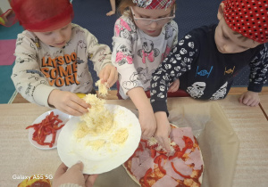 dzieci w kolorowych chustkach na głowie, przy stolikach, samodzielnie przygotowują pizzę.