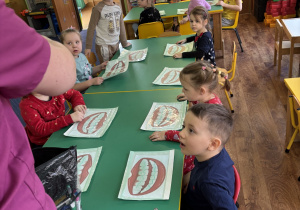 Dzieci siedzą przy stolikach i wykonują zadanie.