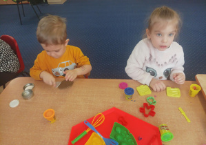 dzieci przy stolikach lepią z ciastoliny, na stolikach leżą kolorowe foremki, pudełka z ciastoliną play doh