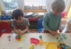 dzieci przy stolikach lepią z ciastoliny, na stolikach leżą kolorowe foremki, pudełka z ciastoliną play doh