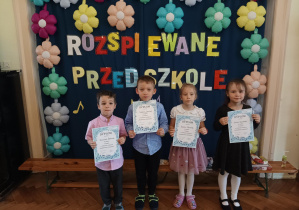 czworo dzieci pozuje do zdjęcia na tle dekoracji z napisem Rozśpiewane Przedszkole