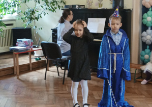 chłopiec i dziewczynka śpiewają piosenkę, pani akompaniuje im na pianinie