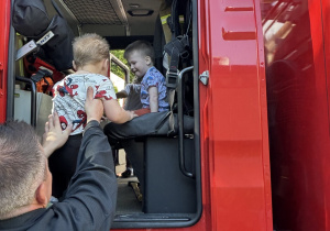 dzieci oglądają wóz strażacki, przymierzają hełm i strój