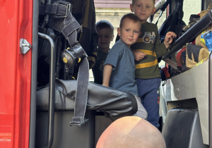 dzieci oglądają wóz strażacki, przymierzają hełm i strój