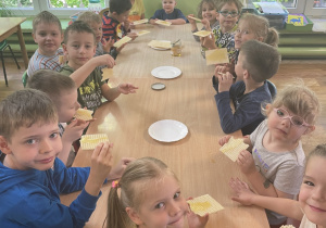 Dzieci siedzą przy stole i zjadają wafle z miodem.