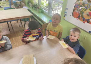 Dzieci siedzą przy stole i zjadają wafle z miodem.