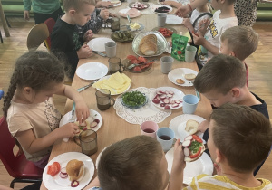 Dzieci siedzą przy stole i przygotowują sobie kanapki.