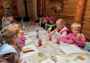 Dzieci siedzą przy stole i jedzą kiełbaski z grilla z pieczywem.