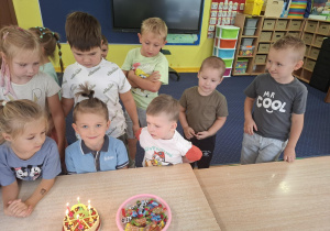 chłopiec świętuje urodziny, dzieci stoją dookoła niego przy stoliku