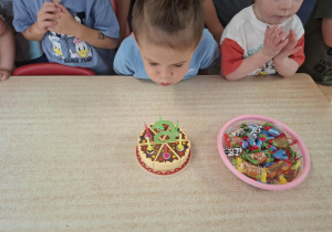 chłopiec świętuje urodziny, dzieci stoją dookoła niego przy stoliku, na którym stoi tort