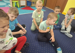 dzieci siedzą na podłodze, na bluzkach mają przyklejone duże, kolorowe kropki