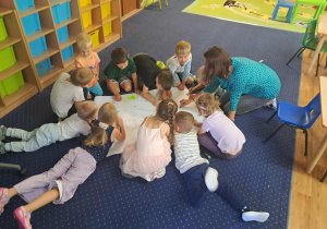 Dzieci na podłodze wykonują pracę plastyczną. W roli głównej kropka.