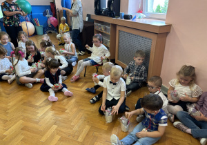 Dzieci siedzą na podłodze i oglądają swoje upominki.