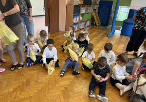 Dzieci siedzą na podłodze i oglądają swoje upominki.