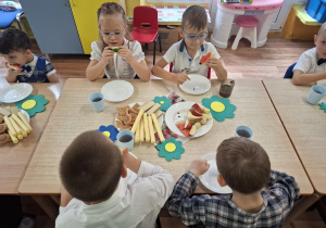 dzieci siedzą przy stolikach, na których są owoce, słodycze, świętują Dzień Przedszkolaka