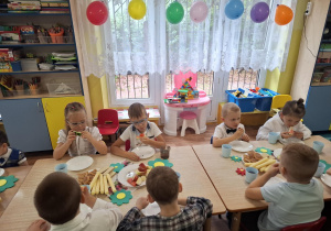dzieci siedzą przy stolikach, na których są owoce, słodycze, świętują Dzień Przedszkolaka