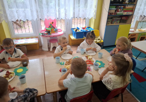 dzieci siedzą przy stolikach, na których są owoce, słodycze, świętują Dzień Przedszkolaka