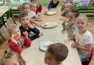 Dzieci siedzą przy stole i zjadają ziemniaczaną przekąskę.