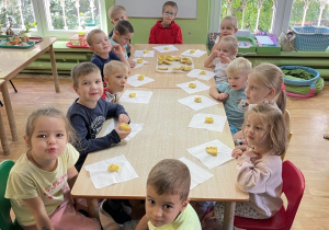 Dzieci siedzą przy stole i zjadają pieczone ziemniaki.