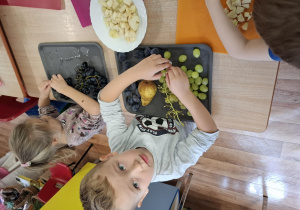 dzieci przy stolikach kroją owoce podczas zajęć kulinarnych