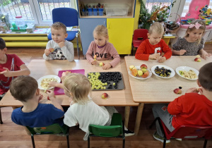 dzieci przy stolikach kroją owoce podczas zajęć kulinarnych
