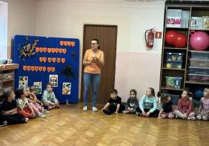 Dzieci siedzą na podłodze i słuchają pani.