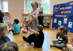 Dzieci siedzą na podłodze i bawią się przy muzyce.