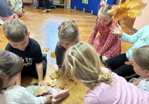 Dzieci siedzą na podłodze i bawią się przy muzyce.