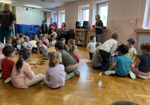 Dzieci siedzą na podłodze i bawią się przy muzyce.