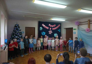 Dzieci na sali gimnastycznej śpiewają piosenkę.