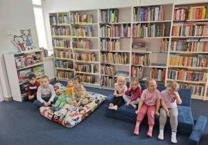 Dzieci siedzą na dywanie w bibliotece.