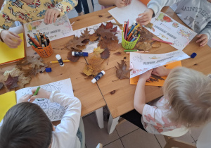 Dzieci stoją wokół stołu i wykonują pracę plastyczną.
