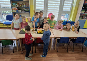 Dzieci stoją wokół stołu na którym leżą warzywa.