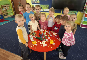 Dzieci stoją wokół stołu na którym leżą warzywne cudaki.