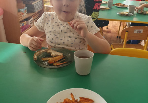 Dzieci siedzą przy stole i degustują frytki, które wykonały.