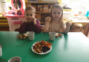 Dzieci siedzą przy stole i degustują frytki, które wykonały.