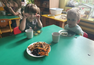 Dzieci siedzą przy stole i degustują frytki, które wykonały.
