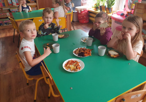 Dzieci siedzą przy stole i degustują frytki, które wykonały.