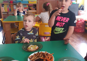 Dzieci siedzą przy stole i degustują frytki, które wykonały.