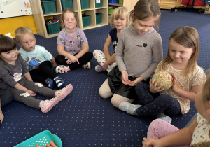 Dzieci siedzą na dywanie i oglądają warzywa.