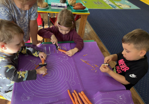 Dzieci siedzą przy stole i obierają warzywa.