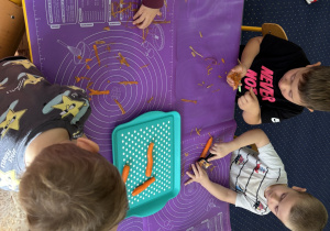 Dzieci siedzą przy stole i obierają warzywa.