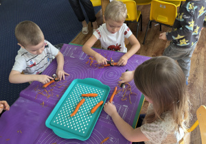 Dzieci siedzą przy stole i obierają warzywa.