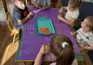 Dzieci siedzą przy stole i obierają warzywa.