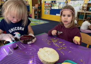Dzieci siedzą przy stole i obierają warzywa.