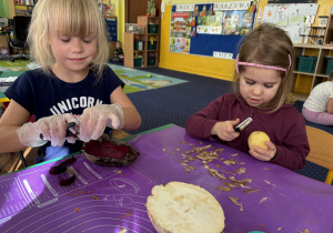 Dzieci siedzą przy stole i obierają warzywa.
